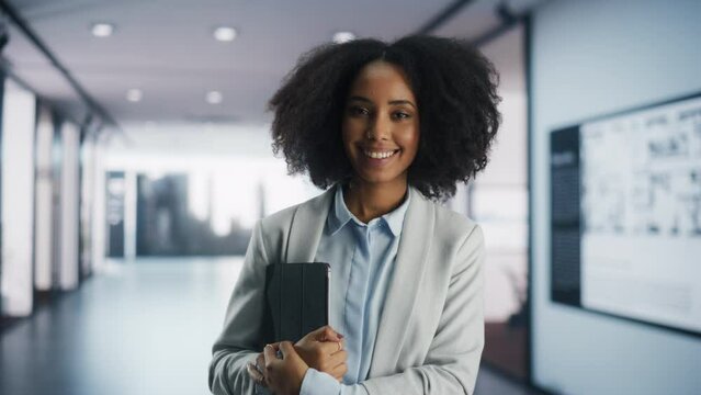 Portrait of a Beautiful African Female Dressed in a Casual Suit Standing in an Office. Young Happy Successful Black Woman Looking at Camera, Posing and Smiling. Girl Working in a Business Company