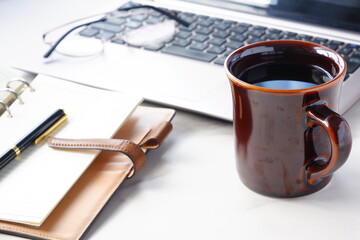 コーヒーを飲みながらノートパソコンでデスクワークをしているイメージ

