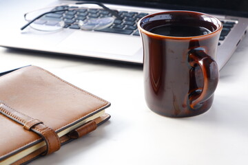 コーヒーを飲みながらノートパソコンでデスクワークをしているイメージ
