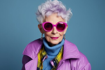 Fashionable senior woman in pink sunglasses. Portrait of a beautiful old lady with purple hair on a blue background.