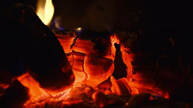 Home cozy evening, slowly burning wood in an old fireplace, smoldering coals and flames on a tree, dim light from the fire, 4k video, background idea about home comfort, footage from a static camera