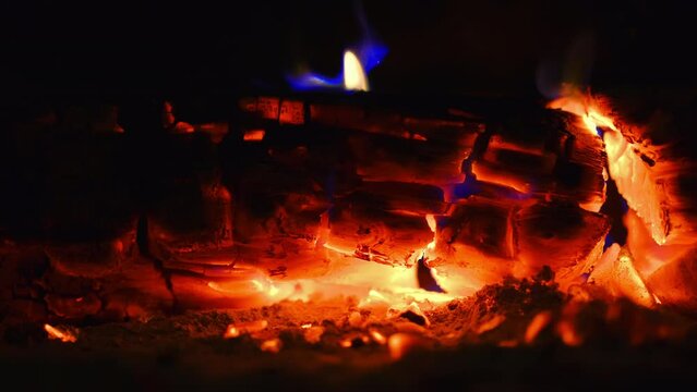 Burning logs in an old fireplace, smoldering coals and flames on a tree, dim light from the fire, 4k video, idea for a background or screensaver about home comfort, footage from a static camera