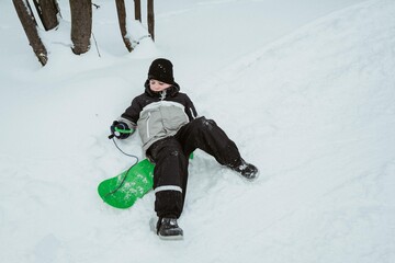 A boy snowboards in a winter snowy forest and falls