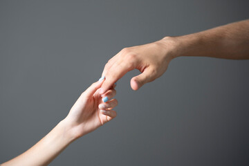 A close-up view captures the tender touch between a mans and a womans hand against a neutral gray...