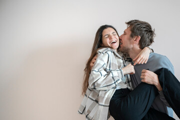 A playful young couple shares an intimate hug while balanced on a chair, their expressions reflecting happiness and affectionate enjoyment.