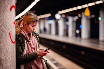 Engrossed in Mobile at the Station, Young woman deeply focused on her phone at the subway station