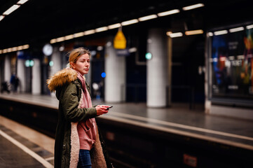 Young Commuter at Subway Platform , Young woman on phone, waiting for her train at a subway station, urban commuting scene
