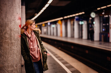 Pensive Wait at Subway Station, Young woman leaning against a pillar, waiting at a subway station