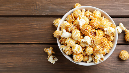 Obraz na płótnie Canvas popcorn with caramel in bowl on wooden background, top view
