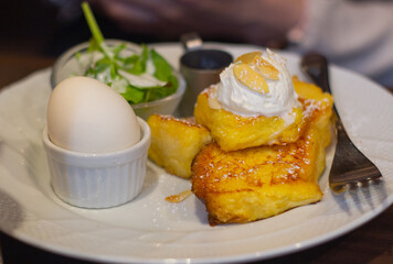 Top down view of french toast served with veggie salad and a boiled egg on plate. Selective focus, blurred background