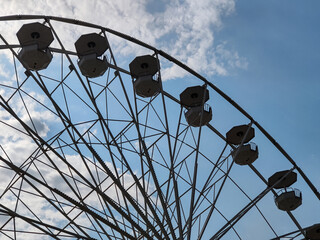 Part of large Ferris wheel against the background of summer  daytime blue sky with clouds. Empty booths, no people. Attraction. Entertainment. Pastime. Vacation. Tourism. Copy space. Selective focus.