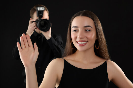 Professional photographer taking picture of beautiful young woman on black background, selective focus