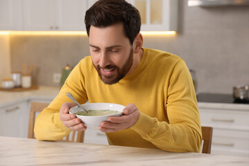 Man enjoying delicious soup at light marble table in kitchen
