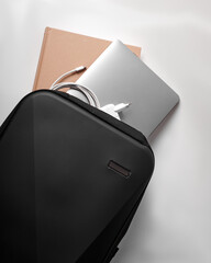 a black backpack with a laptop, charger and notepad lies on a white background, top view