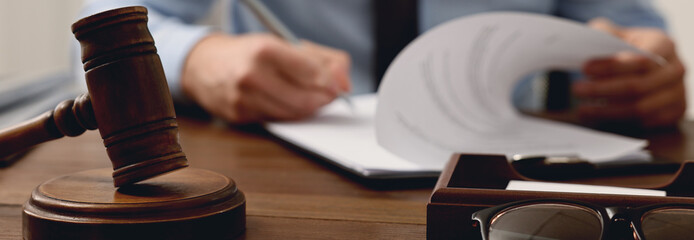Lawyer working with document at wooden table in office, focus on gavel. Banner design