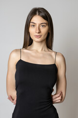 Obraz premium Portrait of a young woman in a black dress on a gray background. Natural female beauty without makeup