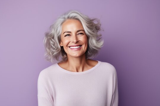 Cheerful mature woman looking at camera with smile while standing against purple background