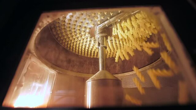 Close looking on the modern mechanism with rotating knife cuts raw spiral shaped macaronis on the equal parts right after automatic manufacturing. Modern food factory technologies in work