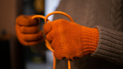 A hand's of a man in orange work gloves untangle orange wire. He wear Synthetic fiber closes