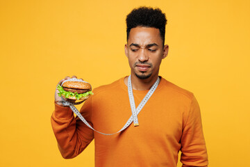 Young man wear orange sweatshirt casual clothes eat hold burger with tied hand by measure tape...