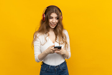 An attractive woman listens to music with red headphones and holds a smartphone. Yellow isolated background