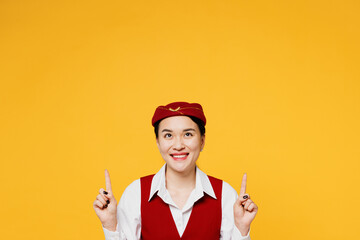 Young stewardess flight attendant woman of Asian ethnicity she wears red vest shirt hat point index...