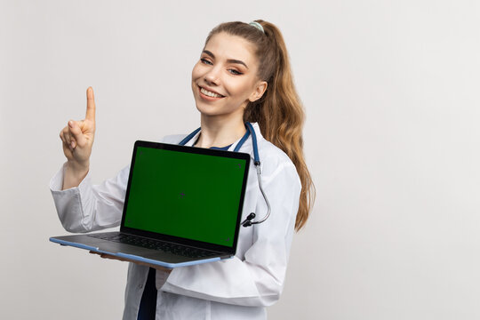 A smiling female doctor in a white coat holds a laptop with a chromakey . The concept of advertising medical services in the hospital. Online consultations