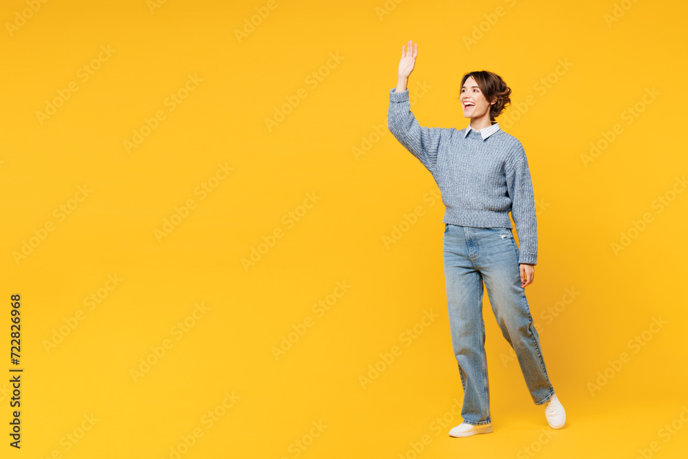 Wall mural Full body smiling happy cheerful young woman she wears grey knitted sweater shirt casual clothes walk go waving hand look aside isolated on plain yellow background studio portrait. Lifestyle concept.