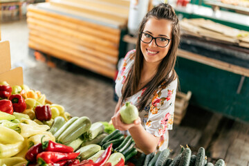 A girl in a white dress carefully chooses an assortment of fresh vegetables, her wooden basket...