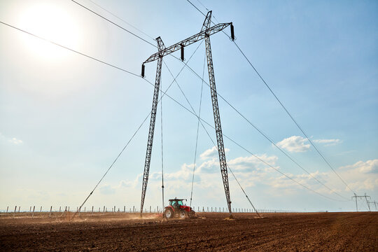 Tractor cultivating field near electricity pylon on sunny day