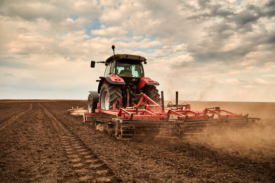 Farmer in tractor with plow cultivating field on cloudy day