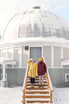Man and woman standing on steps near dome house covered in snow