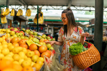 The girl strolls through the market, between stalls with a wooden basket in hands overflowing with an array of fruits and vegetables she has purchased.