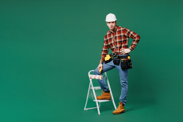 Full body young employee laborer handyman man wear red shirt hardhat put hand on stepladder look...