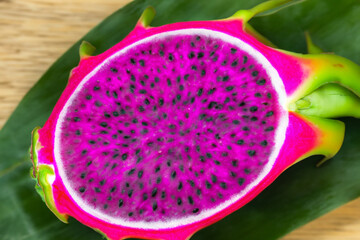 tropical dragon fruit. there is a green leaf on a wooden light table, half of a cut red dragon fruit lies on it, fruit concept