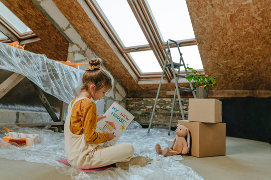 Girl painting in book sitting near skylight window at home