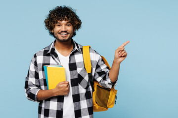 Young Indian boy student he wear shirt casual clothes backpack bag hold books point index finger on area mock up isolated on plain pastel light blue background. High school university college concept.