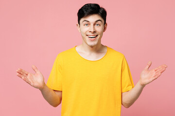 Young surprised shocked excited Caucasian man wears yellow t-shirt casual clothes look camera spread hands isolated on plain pastel light pink color wall background studio portrait. Lifestyle concept.