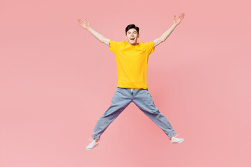 Fototapeta na wymiar Full body young overjoyed fun man he wear yellow t-shirt casual clothes jump high with outstretched hands look camera isolated on plain pastel light pink background studio portrait. Lifestyle concept