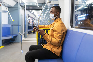 An African-American courier in a protective mask holds a mobile phone while riding in a subway car. Food delivery during a pandemic. Lockdown