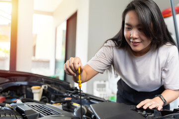 Woman smiles while checking car engine oil. Woman checking car engine oil in the shade working.