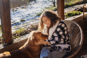 Young adult happy woman cuddling with her dog on the terrace of a country house in early spring