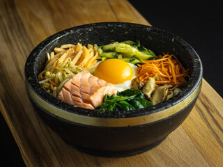 Bowl of korean bibimbap with fried egg, salmon and vegetables