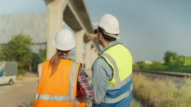 Back view of Two engineers in safety uniform and helmet using tablet discussion and inspection construction process railway. Two engineer working on railway together. Teamwork concept