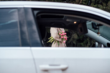 Floral Delivery Services. Order online and get fresh flower special delivery. Faceless woman with bouquet of pink tulip flowers, view from Car Window.