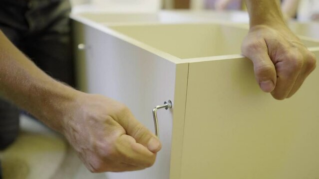 Assembling furniture. Close-up of a hand with a hex wrench tightening a screw on light-colored furniture. Furniture assembler, happy family, moving, mortgage, new house, work with hands, manual labor