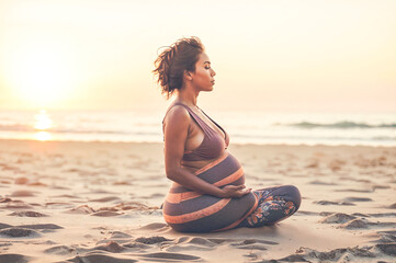 Fototapeta na wymiar A pregnant woman sits on the beach in a yoga pose during sunset.