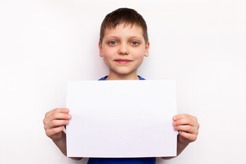 A beautiful little Caucasian boy is holding a blank white sheet of paper with copy space. Portrait of a smiling child isolated on a white background. Banner for advertising campaign