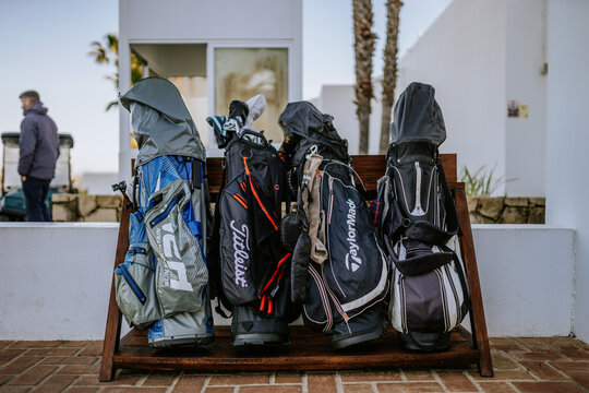 Sotogrande, Spain - January, 23, 2024 -  lineup of golf bags on a bench, with a man in the background at a golf resort.