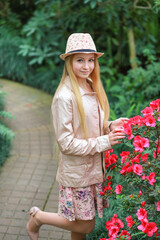 A cute Caucasian girl in a hat walks in a botanical garden in winter where there are bushes with pink azaleas. Beauty and nature. Leisure in the city concept